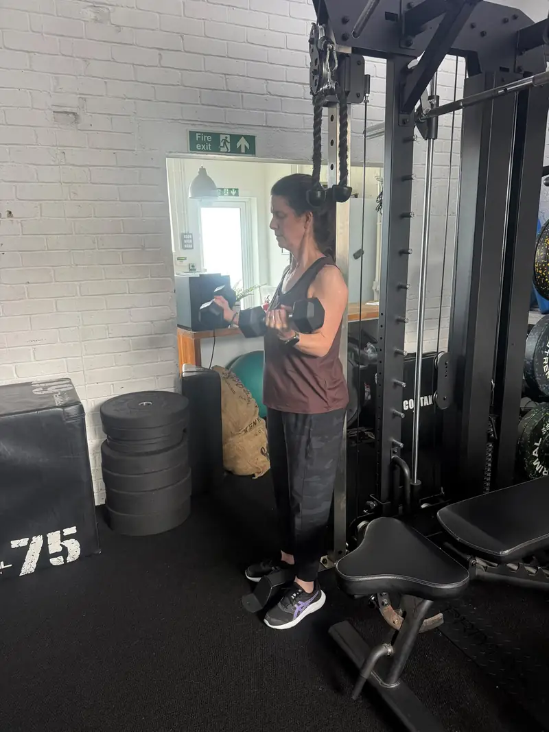 A member doing dumbbell curls by the cable stack