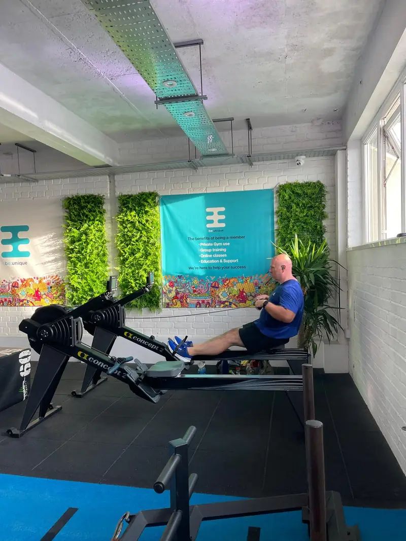 A member on the rower in front of the teal wall